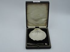 A cased silver scallop shell butter dish of small form having glass liner, trefoil bun feet and