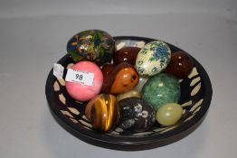 A decorated stone bowl containing various stone and wood sample eggs