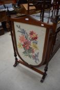 An Edwardian mahogany and inlaid fire screen of shield form with embroidered panel