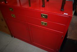 A side cabinet in red finish with campaign style handles, width approx.106cm, locked no key
