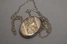 A silver locket of oval form having engraved scroll decoration and silver belcher chain, approx 21.