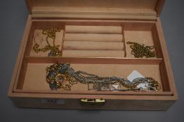 A peach coloured jewellery box containing a selection of costume jewellery chains and necklaces