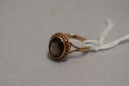 A smoky quartz solitaire dress ring in a collared mount with rope wire decoration on a 9ct gold