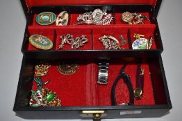 A black jewellery box containing a selection of costume jewellery brooches and watches including