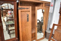 An impressive golden oak Arts and Crafts triple wardrobe having central mirror door and metalwork