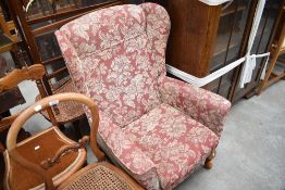 A modern wing-back fireside armchair, upholstered in foliate patterned material, cabriole style