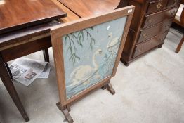 A 1930's oak firescreen/occasional table, the hinged screen with needlework panel over the folding