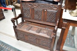 An early 20th Century oak box settle in the traditional style having carving to panels and scroll