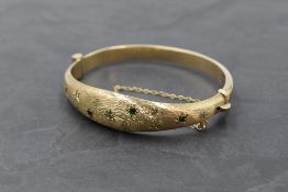 A 9ct gold hinged bangle having diamond and emerald chip decoration in star burst settings on