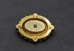 An oval yellow metal brooch having small central diamond and moulded decoration with locket en