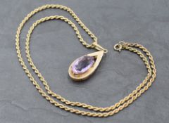 A large amethyst pendant in a yellow metal tear drop shaped open mount stamped 9ct on a 9ct gold