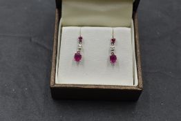 A pair of 18ct white gold stud earrings having a claw set ruby above diamond and ruby drops,