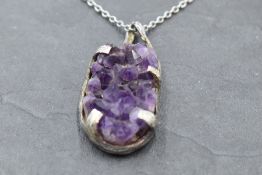 A rough cut oval amethyst pendant in a silver artisan style mount on a white metal chain stamped