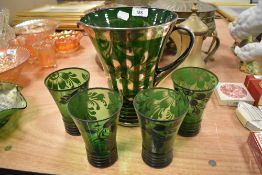 An Edwardian era water jug and glass set in emerald glass with silver floral decoration