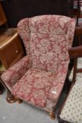 A modern wing-back fireside armchair, upholstered in foliate patterned material, cabriole style