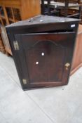 An 18th century oak corner cupboard, with arched panel door opening on brass H-form hinges to reveal