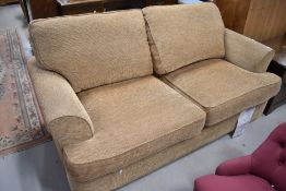 A modern two seater settee, in gold coloured fabric