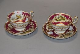 A pair of Victorian porcelain tea cups having hand decorated panels on burgundy ground with gilt