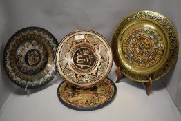 A group of four decorative metal plates, one brass with South American design and three of