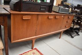 A vintage teak long john style sideboard having triple cupboard and three drawers, stylised legs and