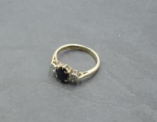 An oval sapphire ring flanked by two diamond chips in illusionary mounts on a 9ct gold loop, size