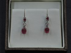 A pair of 18ct white gold stud earrings having a claw set ruby above diamond and ruby drops,