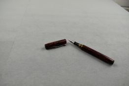 An unnamed leverfill fountain pen in black and red wood grain design having brass thread for cap