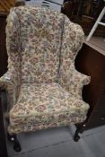 A period wing back armchair in the Queen Anne style, having later upholster and raised feet