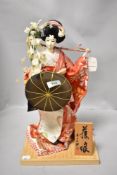 A oriental doll on display stand and similar pin cushion.