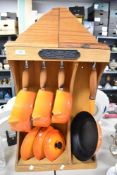 A wooden La Crueset rack of Volcanic orange pans of which there are three saucepans and a skillet.