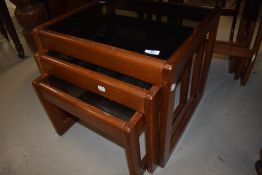 A nest of mid century teak tables with glass top