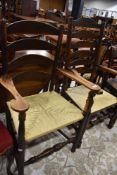 Two period oak ladder back carver chairs having later rush seats