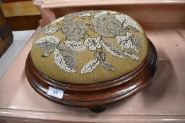 An early Victorian footstool in button design with mahogany frame on turned feet with bead work top