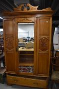 An early 20th century pine wardrobe having carved panels and cornice with mirror centre door