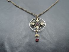 An Edwardian style yellow metal pendant having a central ruby in foliate surround with ruby drop, on