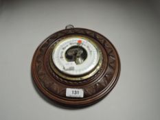 An Edwardian aneroid barometer having carved button form oak frame with enamel dial