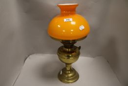 An early 20th century oil lamp having brass body and orange glass shade