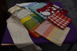 A collection of colourful, predominantly 1940s and 50s table cloths and an embroidered apron.