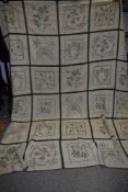 A large antique bed throw having green cross stitch embroidery and crotchet panels and edging.