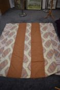 A large antique bed throw using bands of copper fabric spaced between bands of colourful abstract