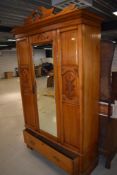 An early 20th century pine wardrobe having carved panels and cornice with mirror centre door