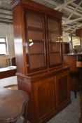 A Victorian mahogany bookcase over cupboard, having moulded cornice and plain frieze over two arched