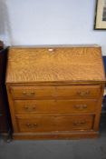 An Edwardian light oak bureau with three chamfered edge long drawers, the fall front opening to