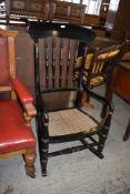 A Victorian black painted or ebonised cane seated rocking chair, the arched top rail over turned