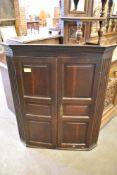 A George III oak corner cupboard having canted and fluted ends enclosing triple panelled doors.