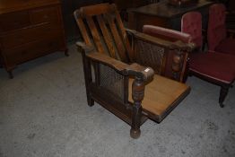 An early 20th century oak reclining armchair, the reclining action between cane panelled arms with
