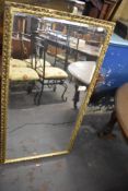 A large gilt framed and bevelled mirror. 128CM. X. 67CM. Some losses.