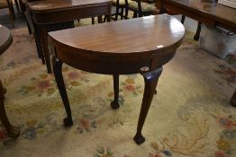 A 1920s demilune foldover card table raised on cabriole type supports terminating in claw and ball