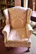 A 20th century wingback armchair of Georgian design, having shaped wings and scrawled out arms