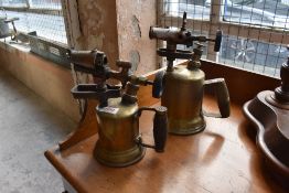 Two vintage brass blow torches of traditional design.